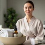 A young adult in a modern spa lounge with a towel and an amber essential-oil bottle in the foreground, suggesting intentional self-care treatments.